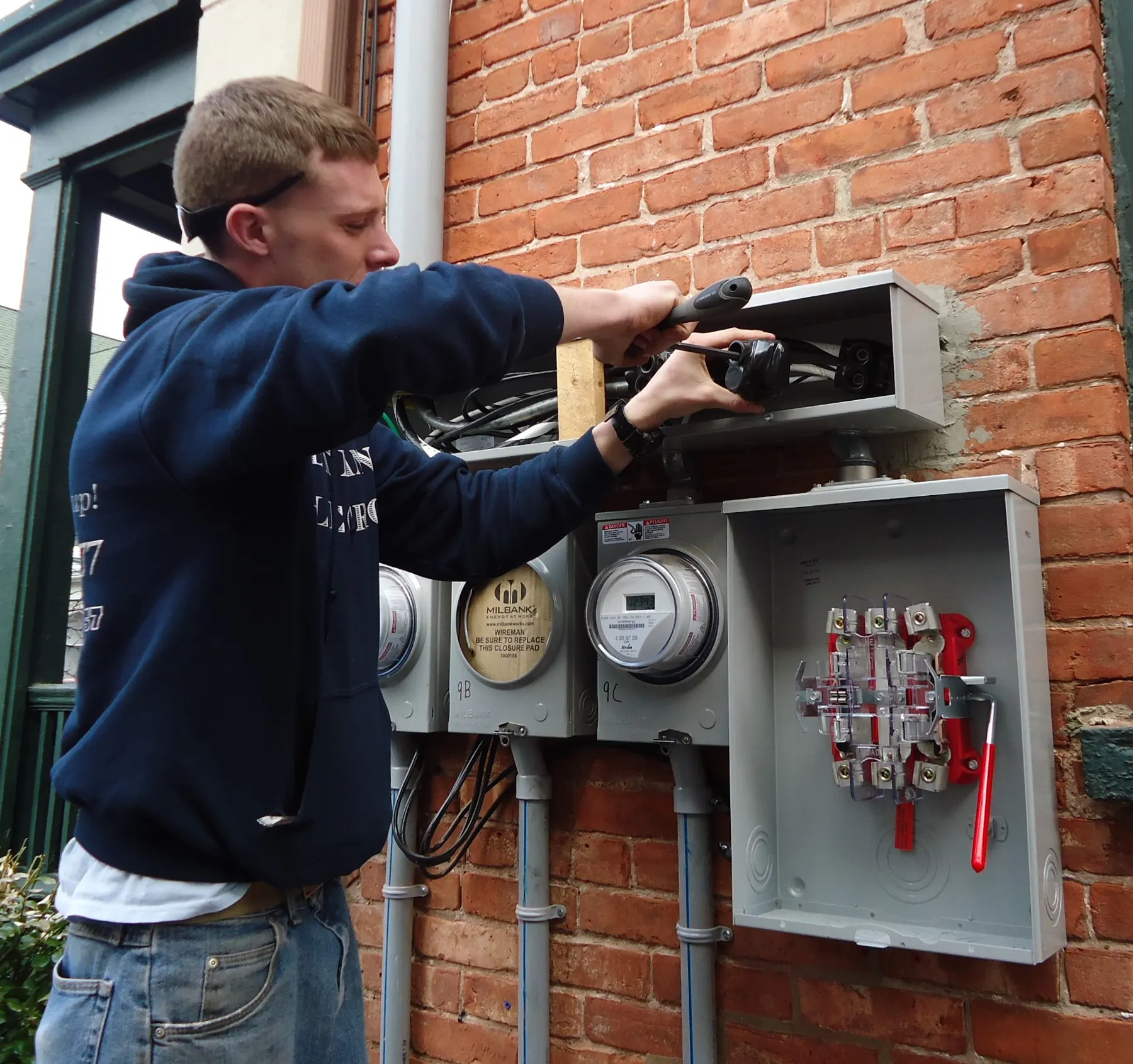 Electrician wiring an outdoor service box on the side of a brick building